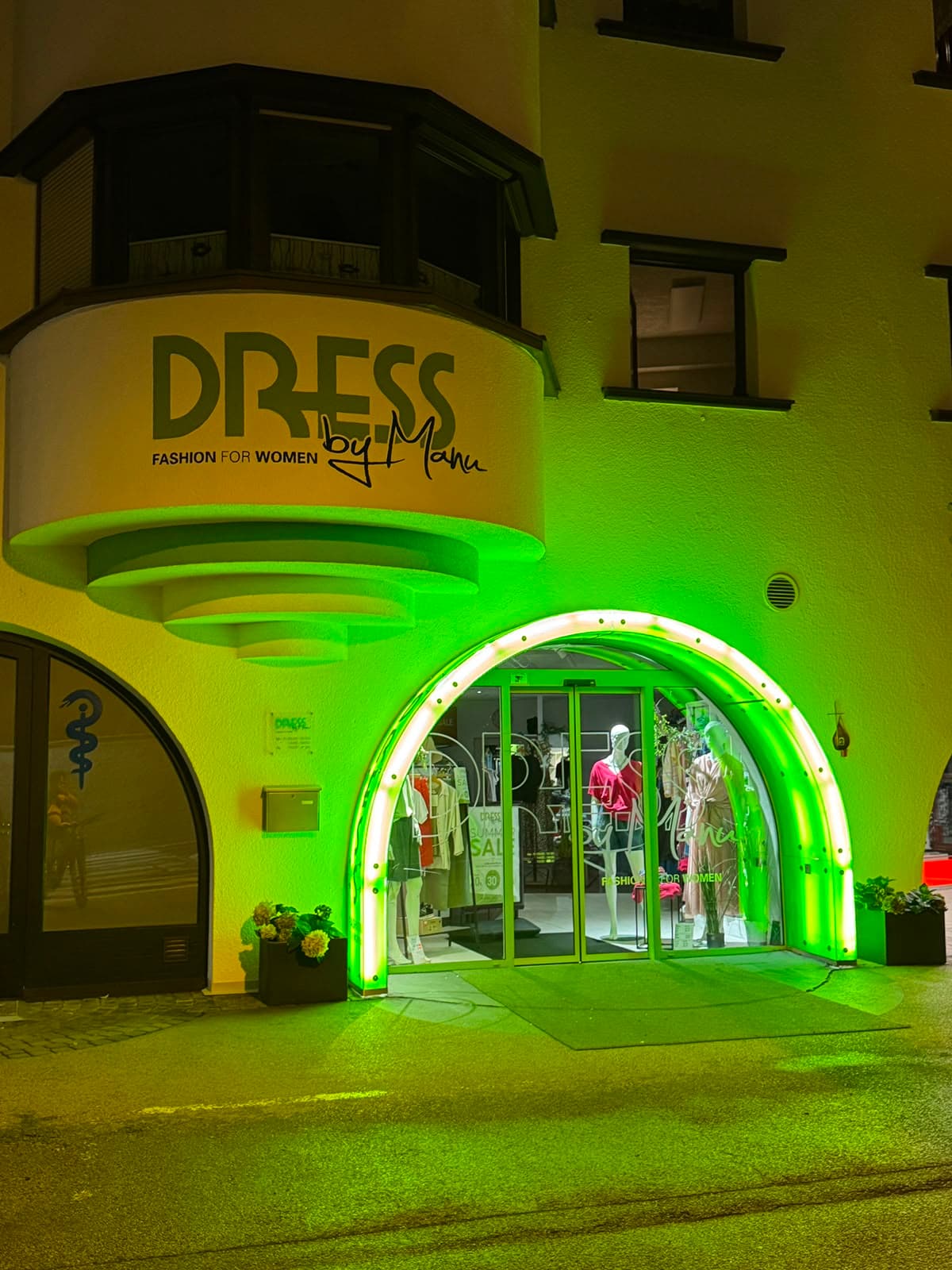 Grün beleuchteter Eingang der Boutique DRESS by Manu in Oetz mit Schaufensterpuppen